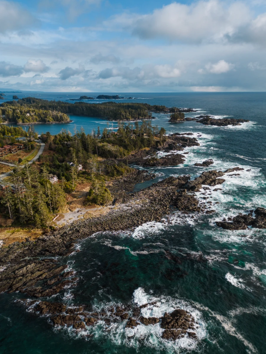 Several sections of white frothy waves are created by strong waves crashing into rocky outcrops along the rocky shore near Ucluelet