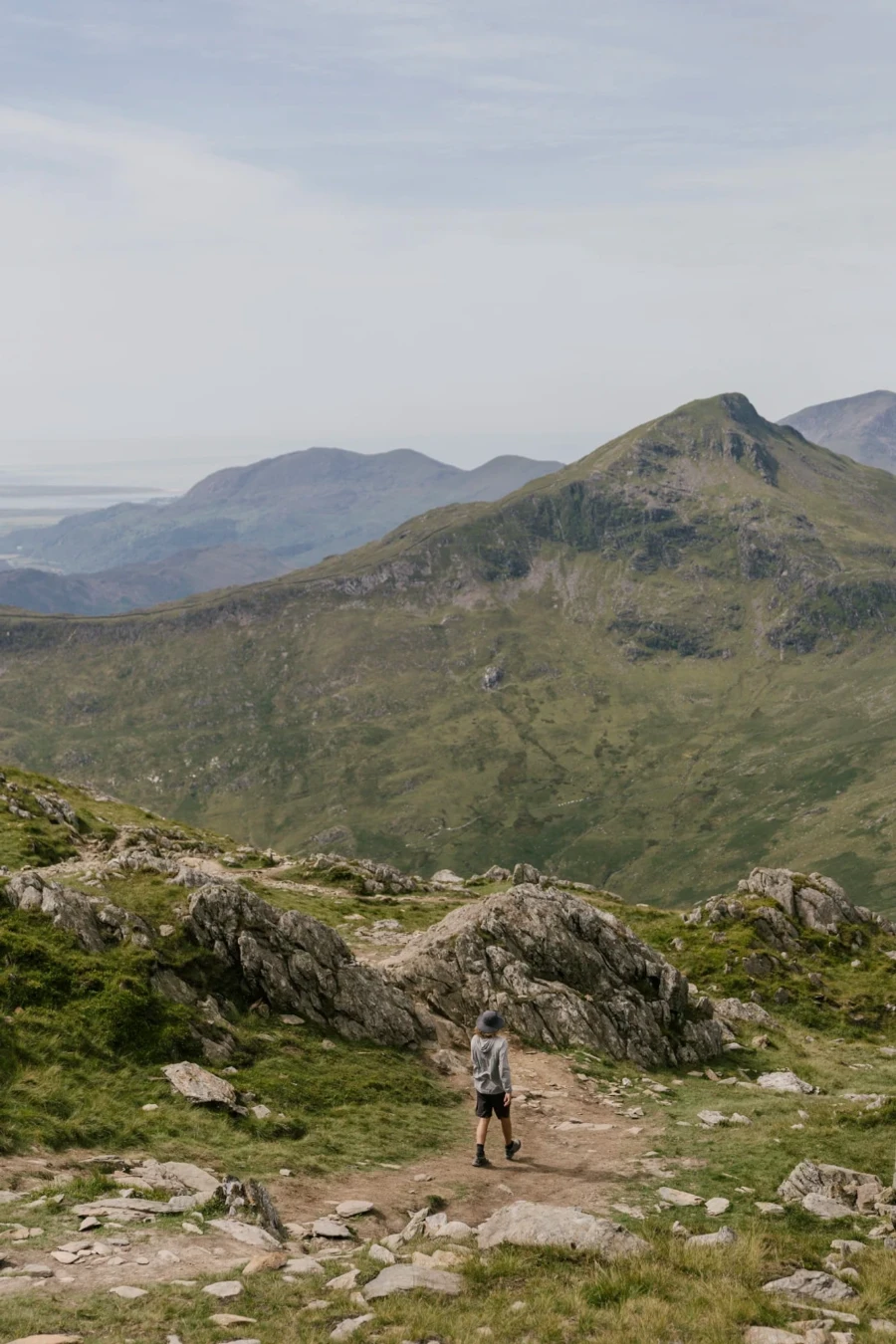 A man is walking downhill along a dirt path next to scattered rocks on Mount Snowdon, Wales
