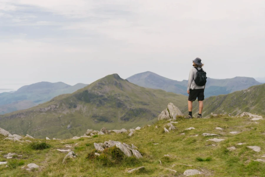A man standing on a grassy hill looking out to mountain peaks on the horizon in Snowdonia, Wales