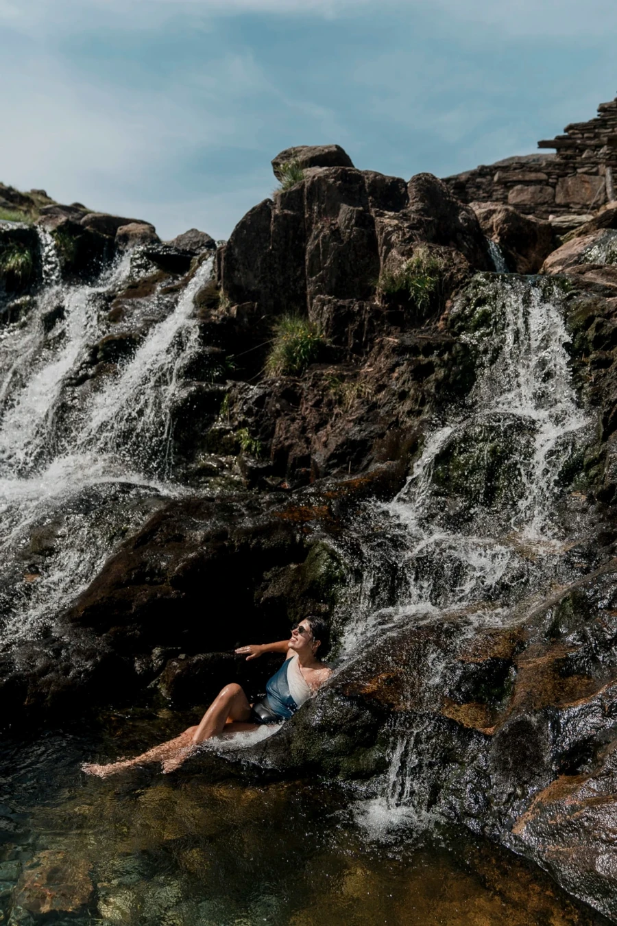 A woman sitting in a shallow pool of water while two waterfalls fill the pool on either side of her