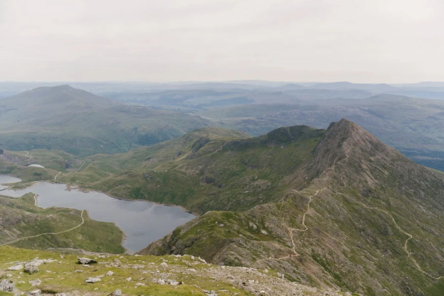 A long thin dirt path climbs up the side of a mountain then continues along the ridge with a large lake on the other side