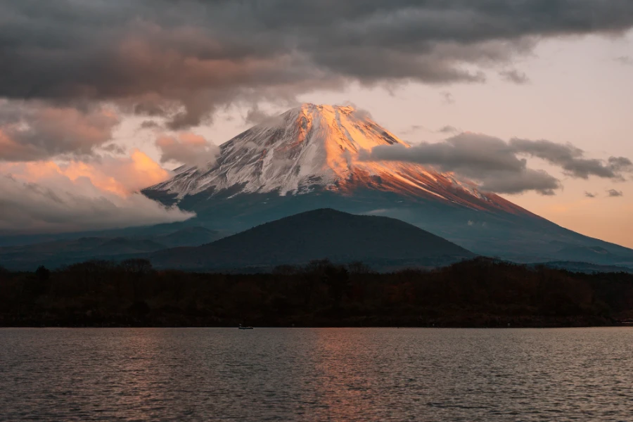 A few small clouds surround the snowy peak of  Mt. Fuji at sunset Japan
