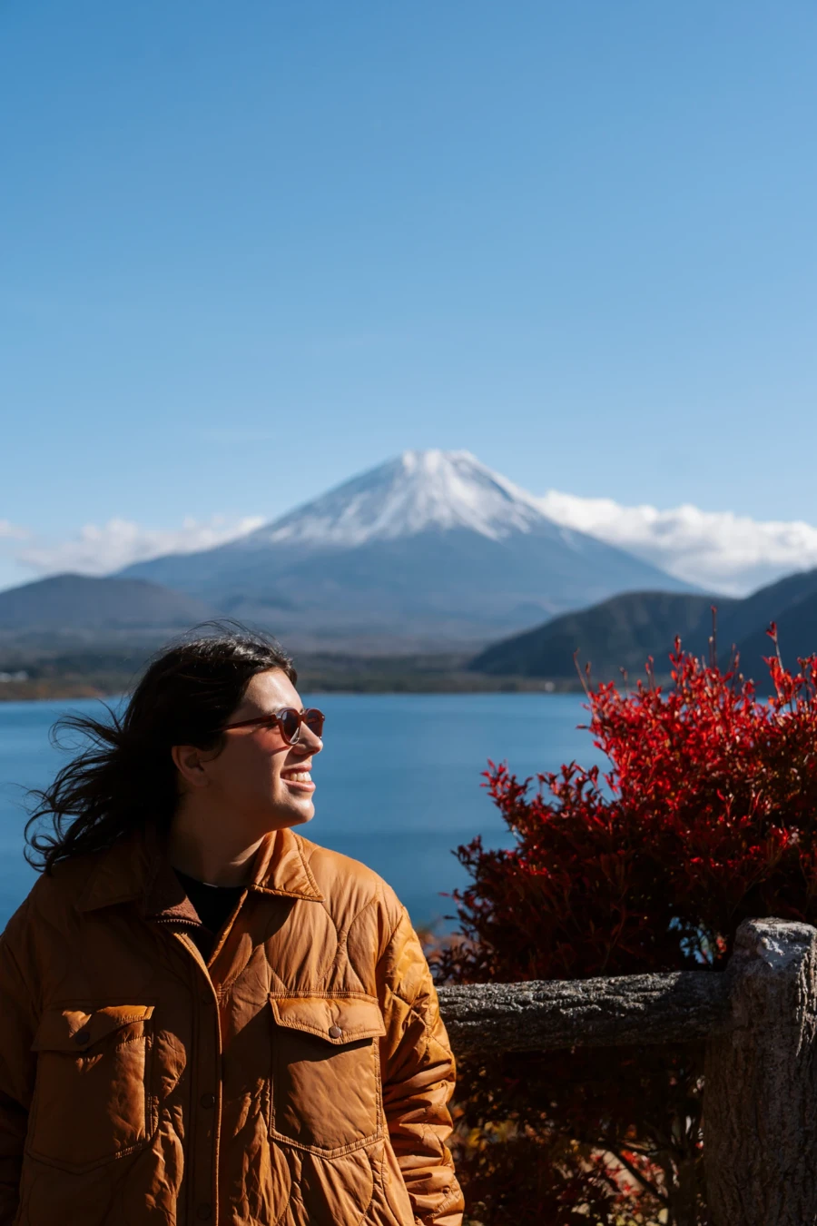 A woman stands at a viewpoint above Lake Motosu with Mt Fuji on the horizon behind her