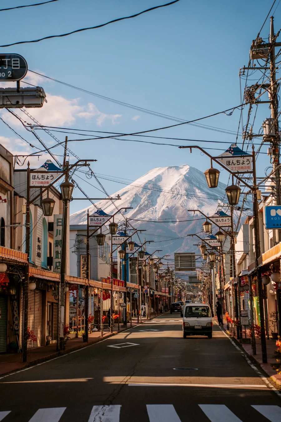 A small Japanese truck drives down a lantern lined street that leans to a view of Mt Fuji on Honcho Street (Fujiyoshida)