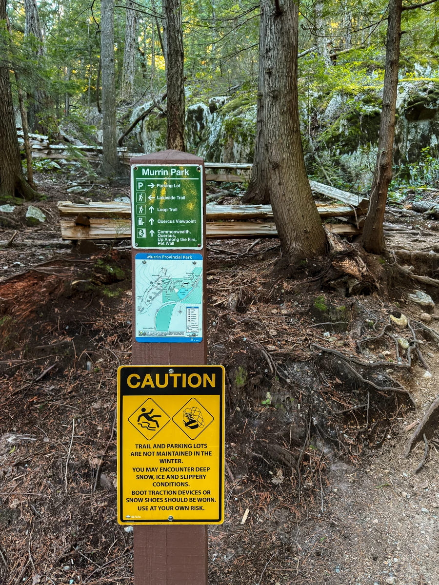A wooden post has several warning signs as well as a trail map at the trailhead of the Murrin Park Loop