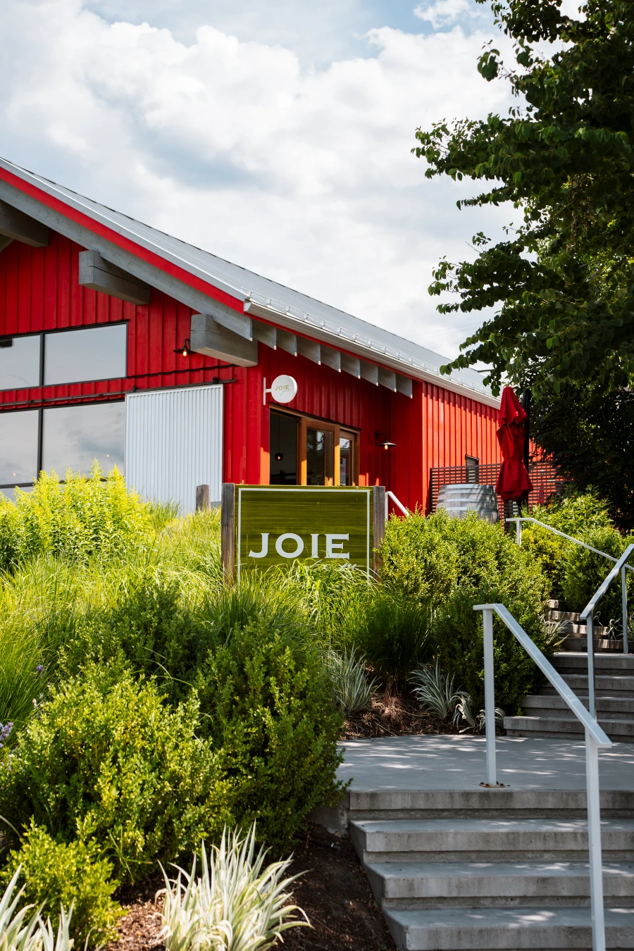 Stairs lead up to a large red metal barn with a sign in front that reads ‘Joie’