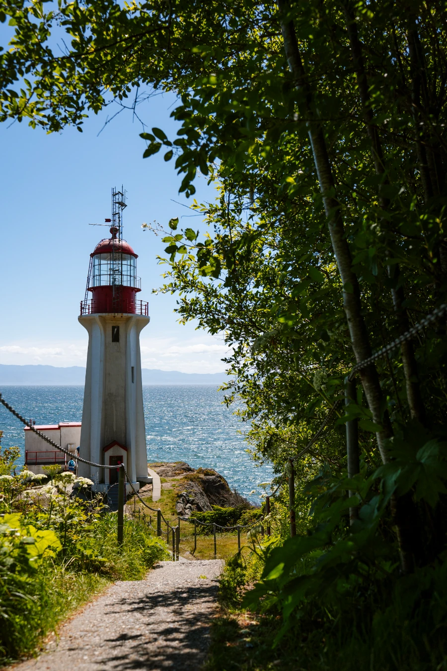A flat narrow gravel path leads to a white and red lighthouse in Juan De Fuca