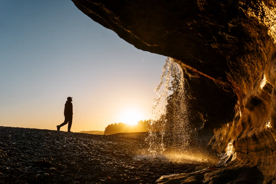 A steady stream of water is pouring over a sandstone cliff onto the rocky beach below