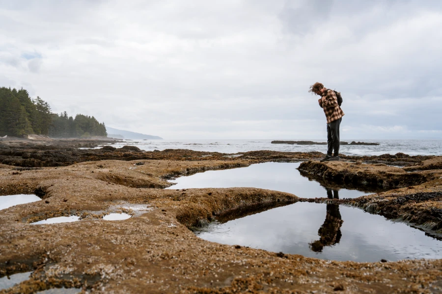 A man stands above a large tidal pool at Botanical Beach with a clear reflection