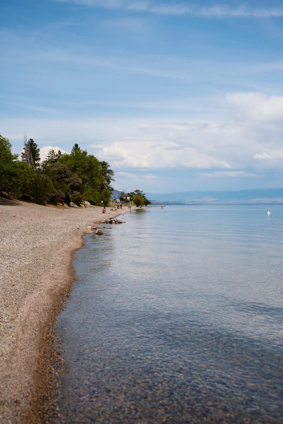 A long gravel beach runs along next to the calm waters of Okanagan Lake