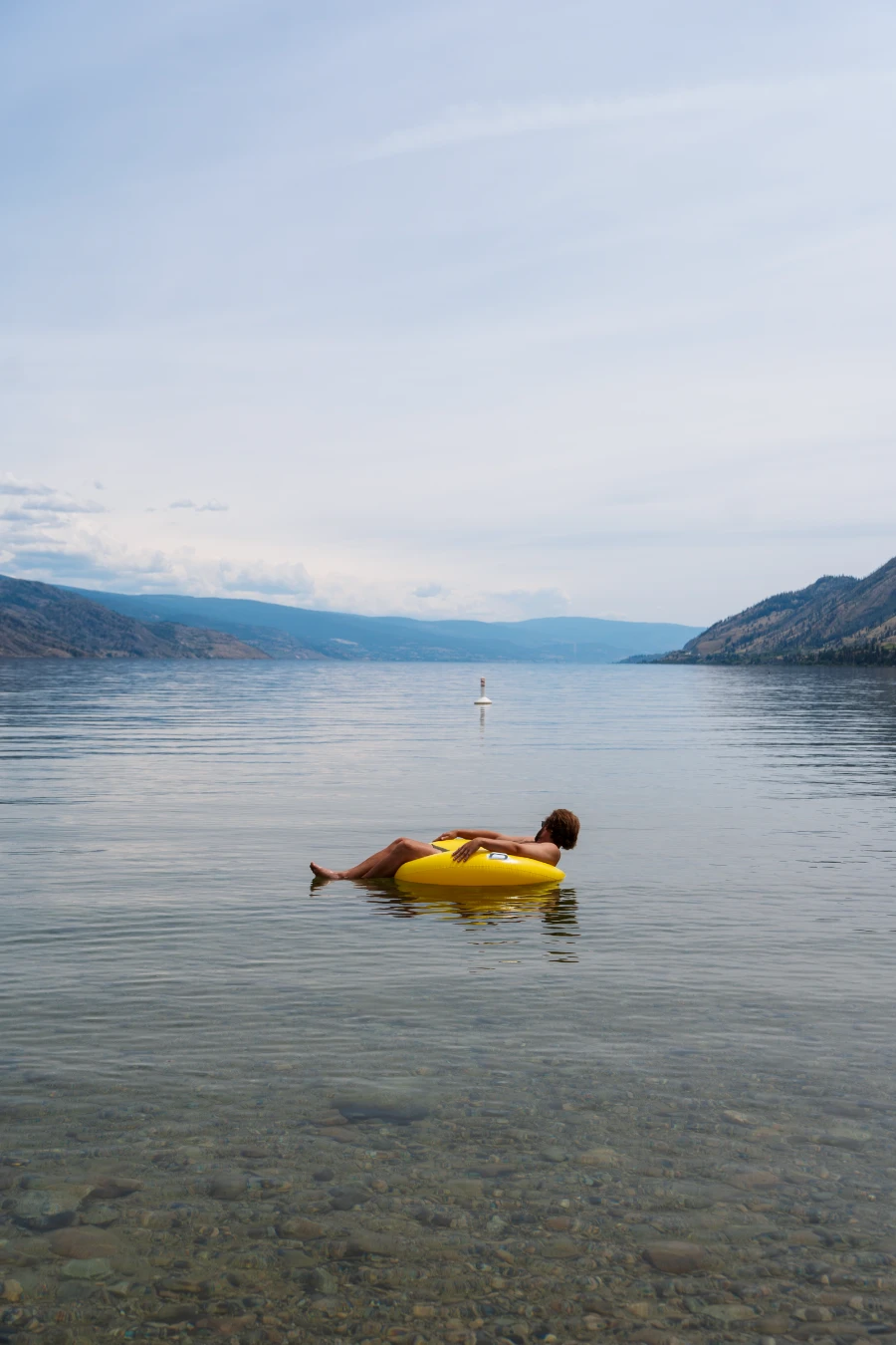 A man floats in a small yellow inflatable tube on the calm waters of Okanagan Lake