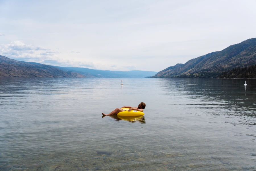 A man floats in a small yellow inflatable tube on the calm waters of Okanagan Lake