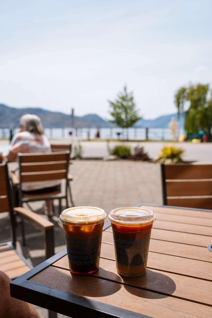 Two iced coffees in plastic cups on a wooden table on an outdoor patio at Bliss Bakery in Peachland