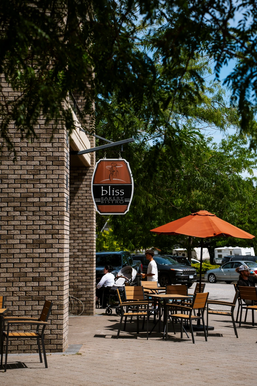 Several patio tables and chairs scattered across a wide walkway with a sign hanging off a building that read ‘Bliss Bakery Bistro’