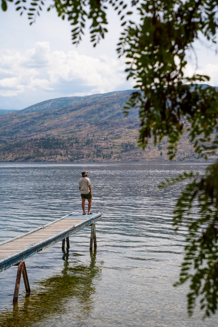 A man standing on the end of a narrow, worn dock that stands above shallow water