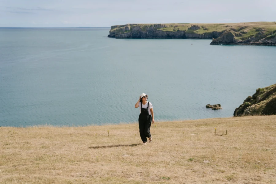 A woman walks along a dry grassy cliff in front of the sea near Barafundle Bay