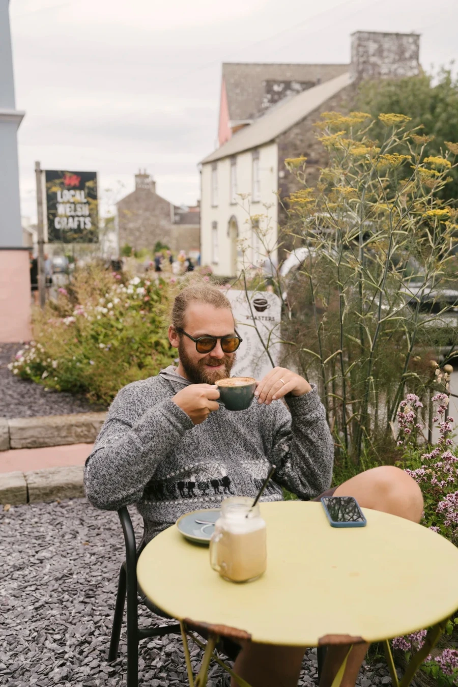 A man sitting at a small table sipping a large coffee in St Davids, Wales