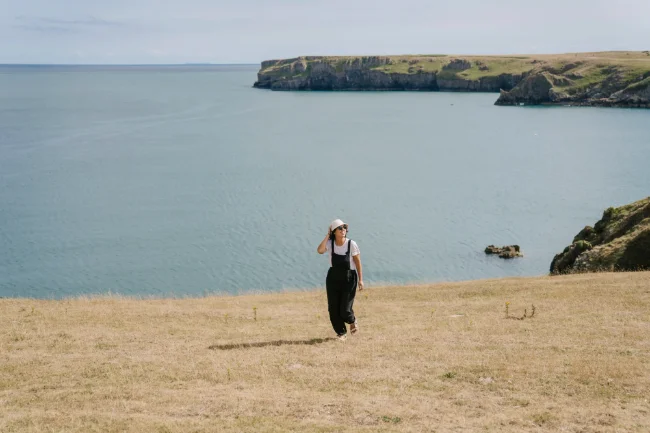 A woman walking away from the sea along a dry grassy cliff in Wales