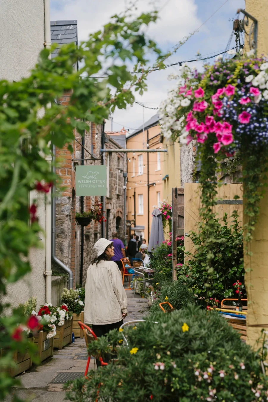 A woman walking down a narrow flower lined street