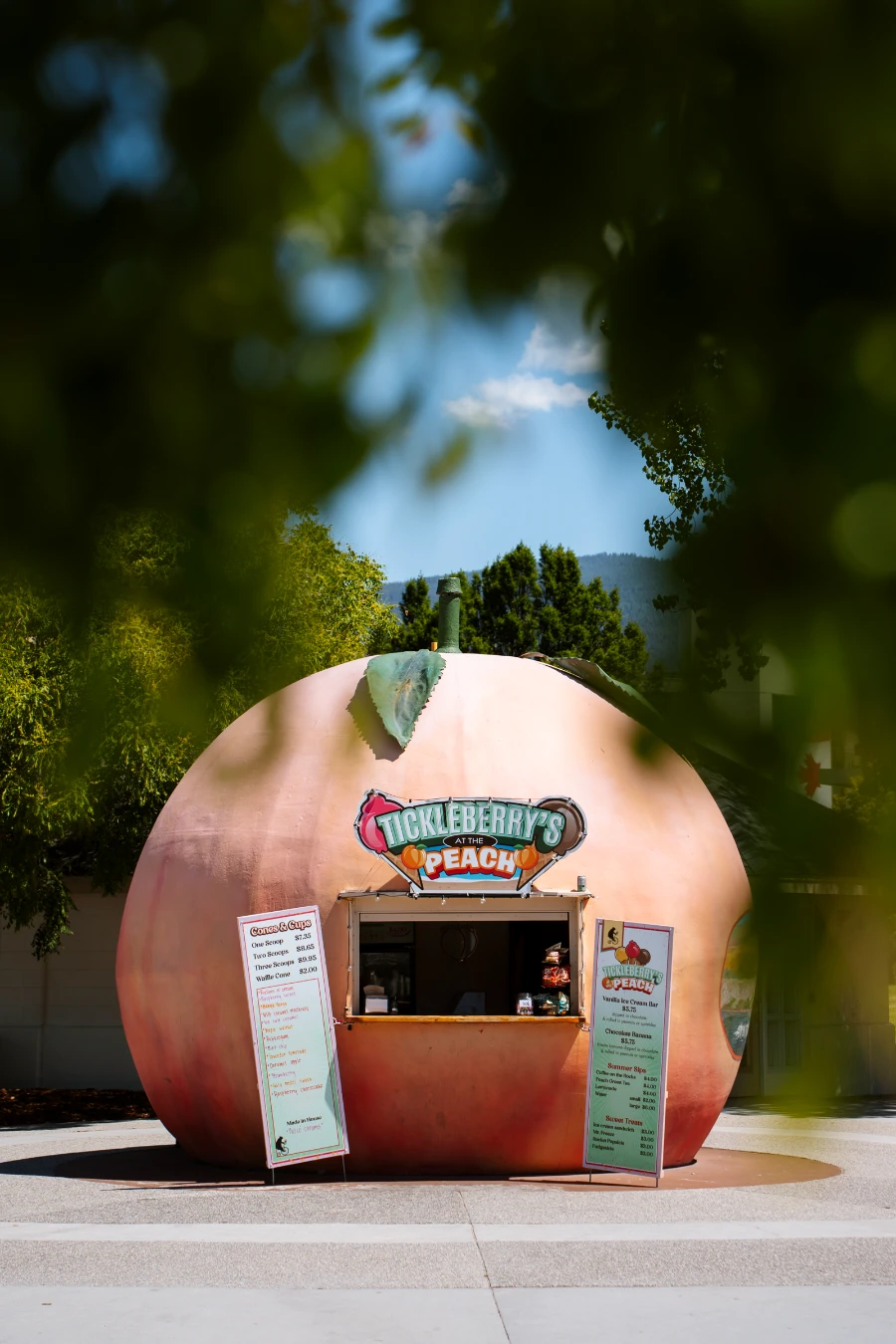 A dome-shaped and colored to look like a peach has a small kiosk-style opening in it above which a sign reads ‘Tickleberry’s Peach’