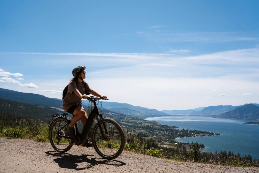 A woman riding an E-bike along the gravel KVR trail outside of Penticton looks down at Okanagan Lake far below her.