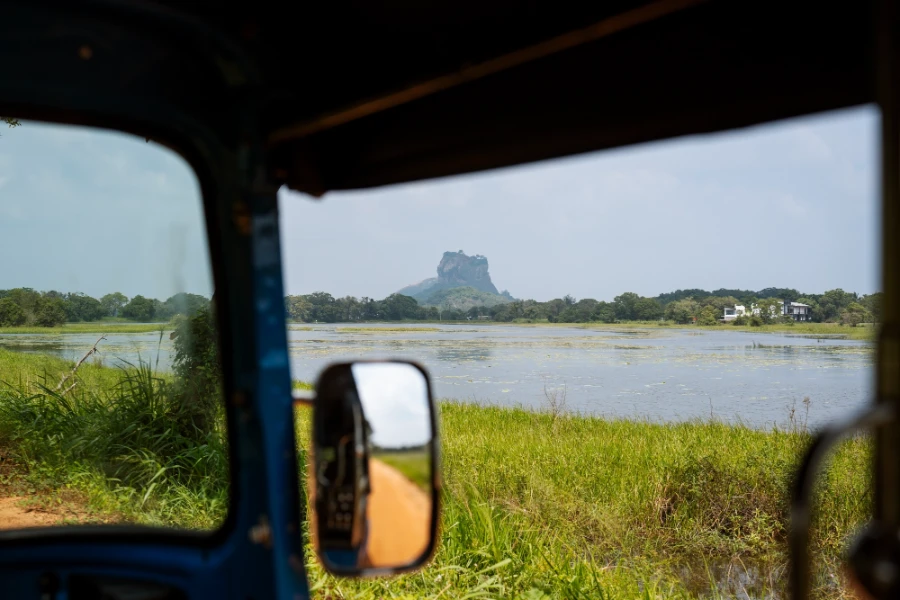 The granite cliffs of Lion's Rock past a large lake through the window of a tuktuk