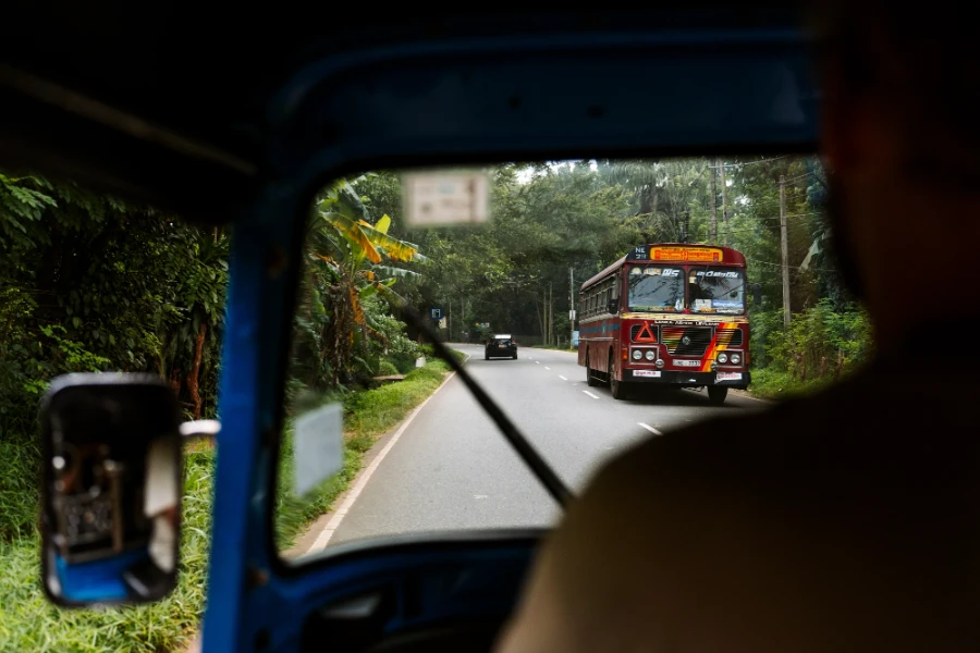A colorful bus framed through a tuktuk windshield on a paved jungle road in Sri Lanka