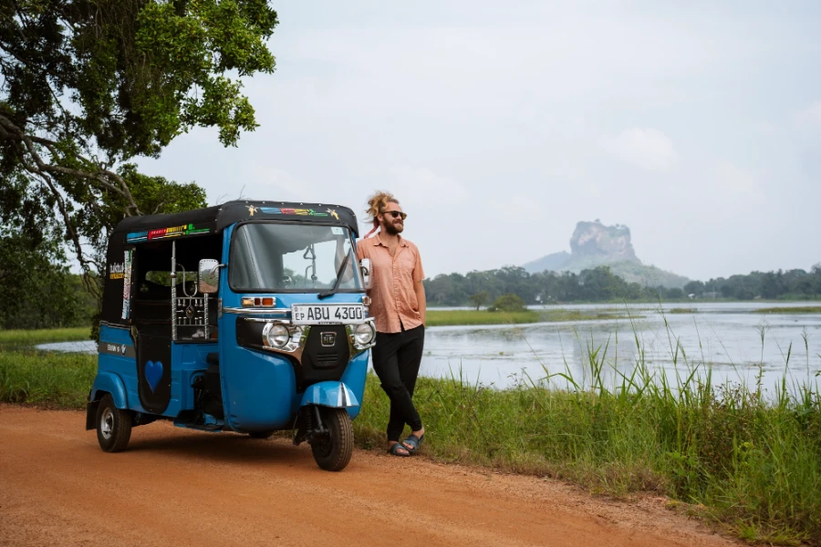 Man standing next to a tuktuk with Lion Rock in the background