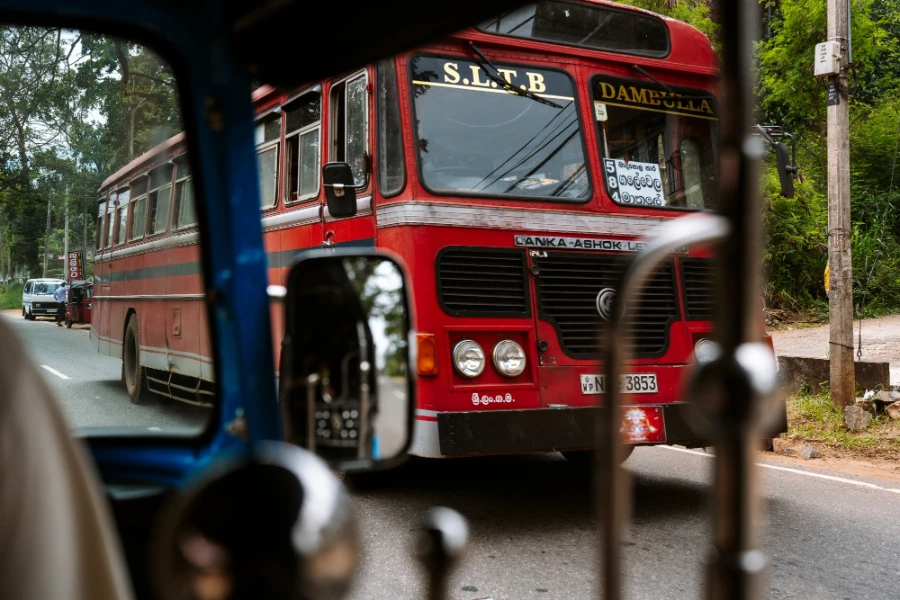 A big red bus framed through the window of a tuktuk driving down a country road in Sri Lanka
