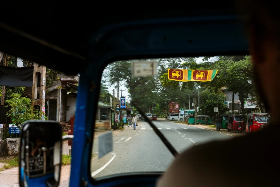 A small town street framed through a tuktuk windshield with Sri Lankan flags hung across the street