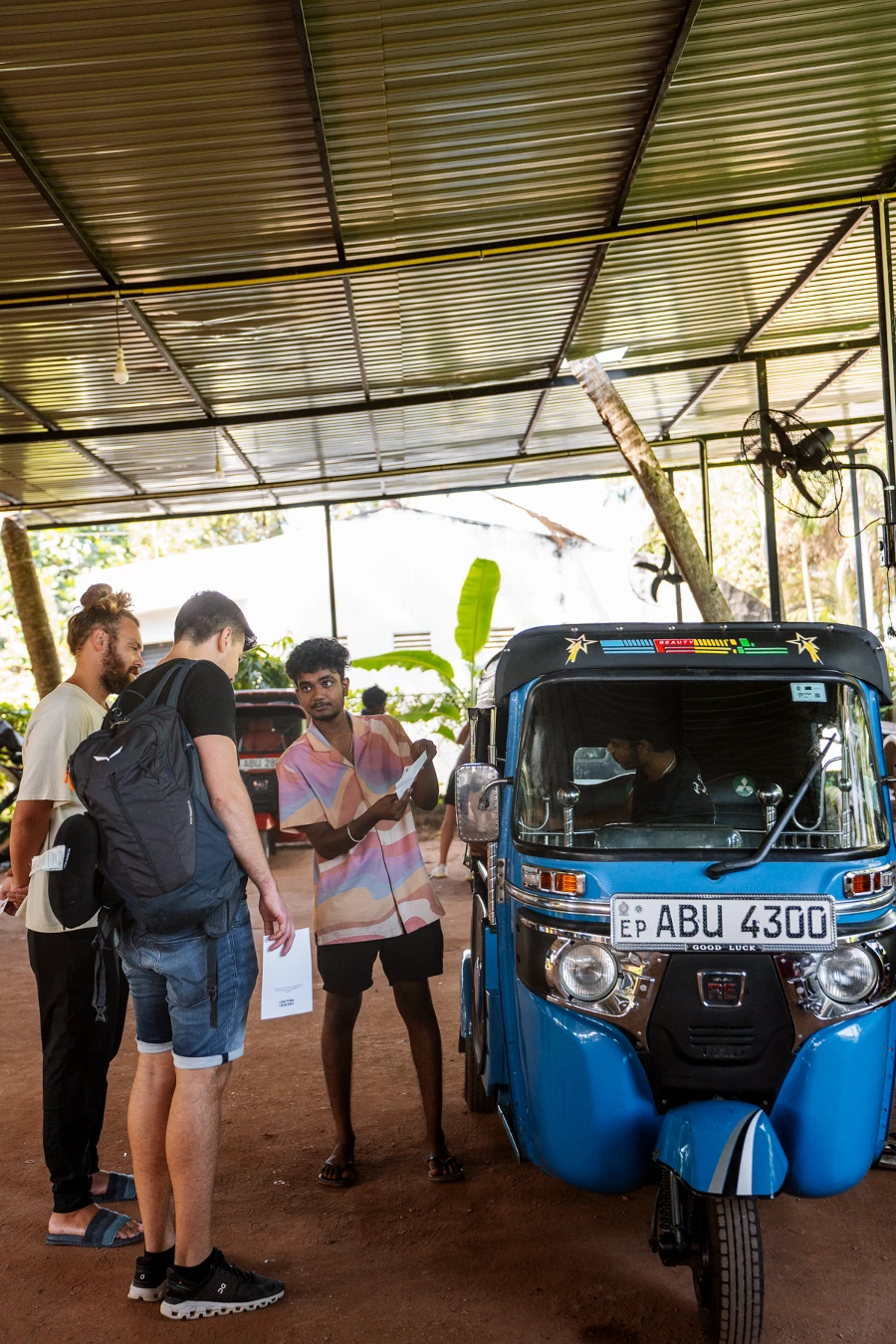 One man showing a piece of paper to two other men next to a blue tuktuk