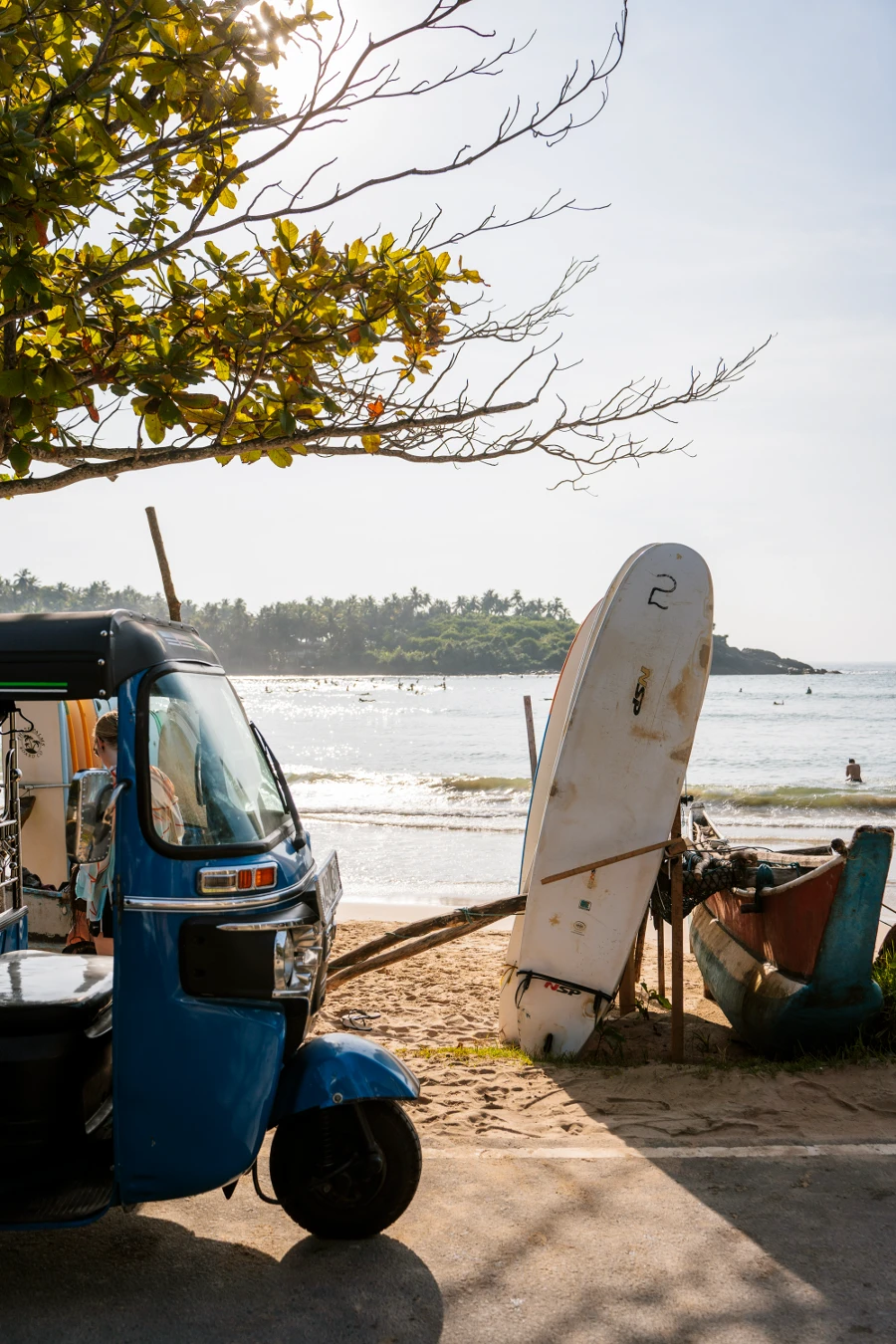 A tuktuk parked next to a stack of surfboards on the beach in Hiriketiya, Sri Lanka