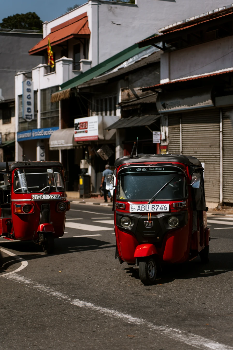 Two red tuktuks make a right turn on an empty street