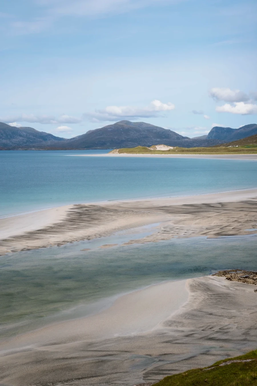 The long white sandbars of Seilebost Beach are exposed at low tide with mountains dotting the horizon