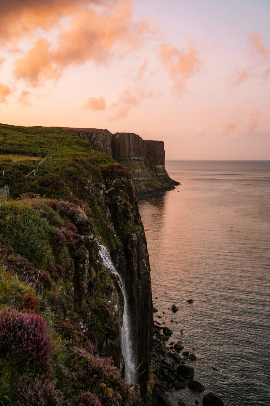 Mealt Falls pours over Kilt Rock and into the sea below that is glowing a faint orange color in the sunset light