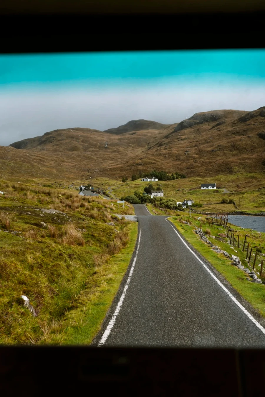 A narrow single track road leading to a small cluster of white cottages