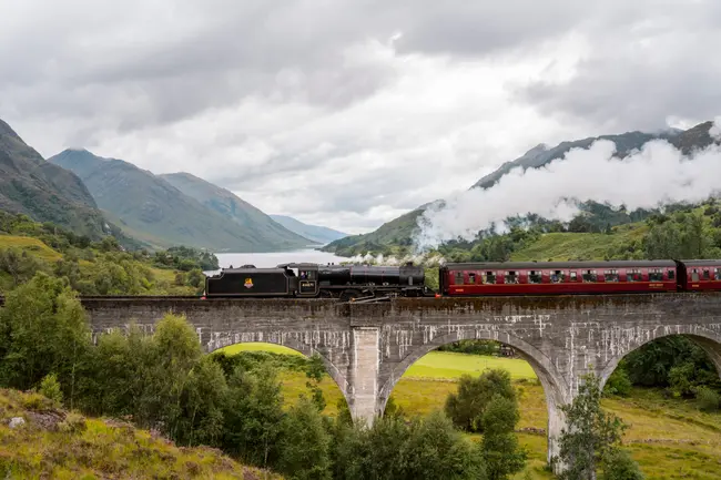 An old train leaves a trail of steam behind it as it runs along a multi-arched stone bridge