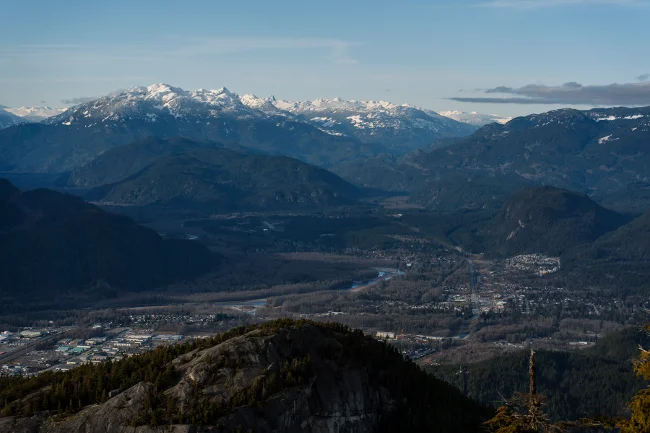 A distant view of a dry Squamish Valley with the snowy peaks of the Tantalus range in the distance