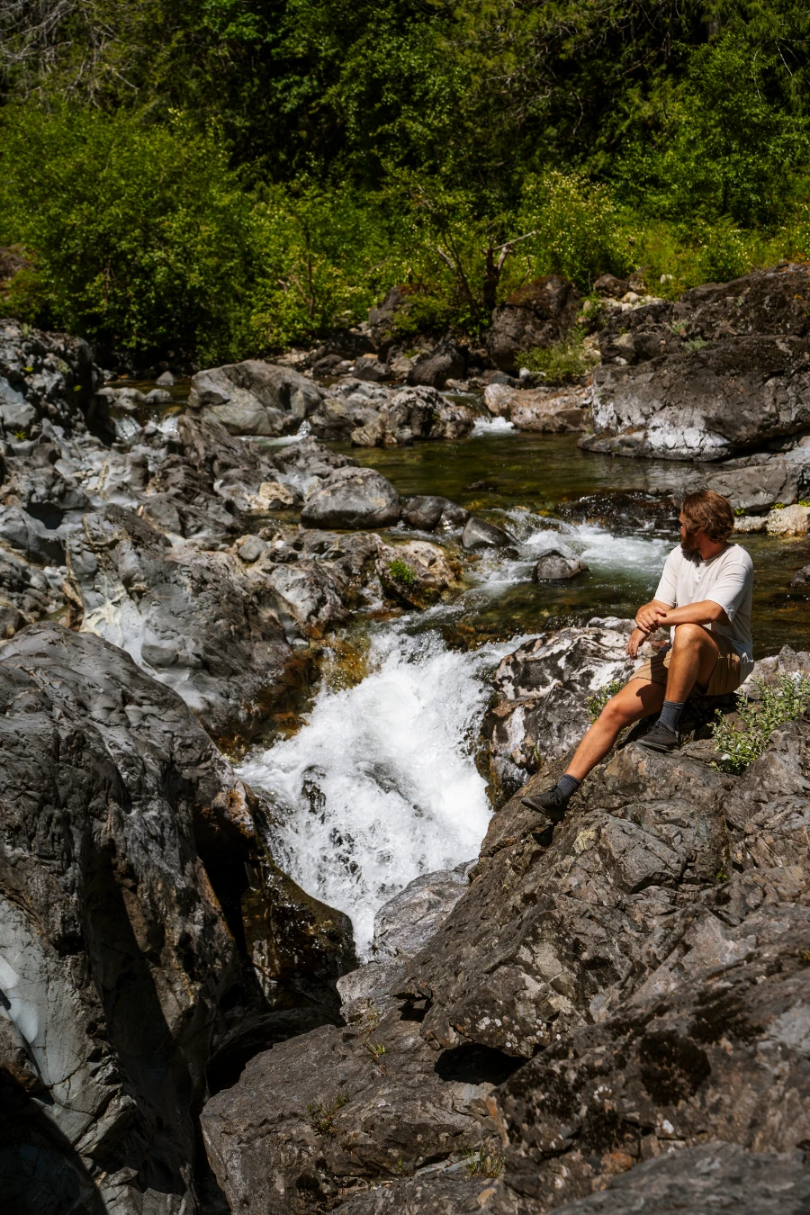 A man sits on a rock next to a narrow canyon with a large and powerful waterfall pouring in at Sooke Potholes Provincial Park