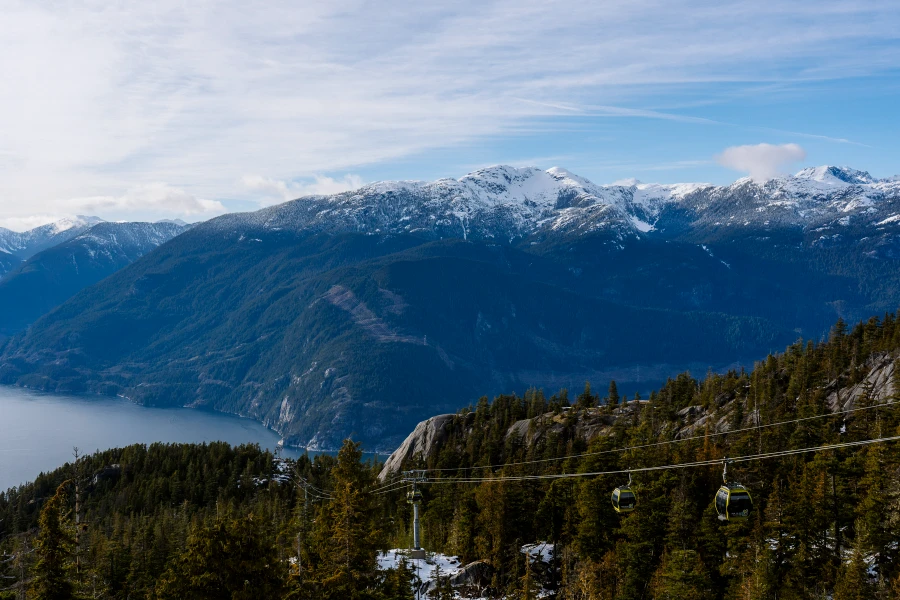 Gondolas coming up and down a forested mountainside with distant snowy peaks visible in the distance in Squamish, BC