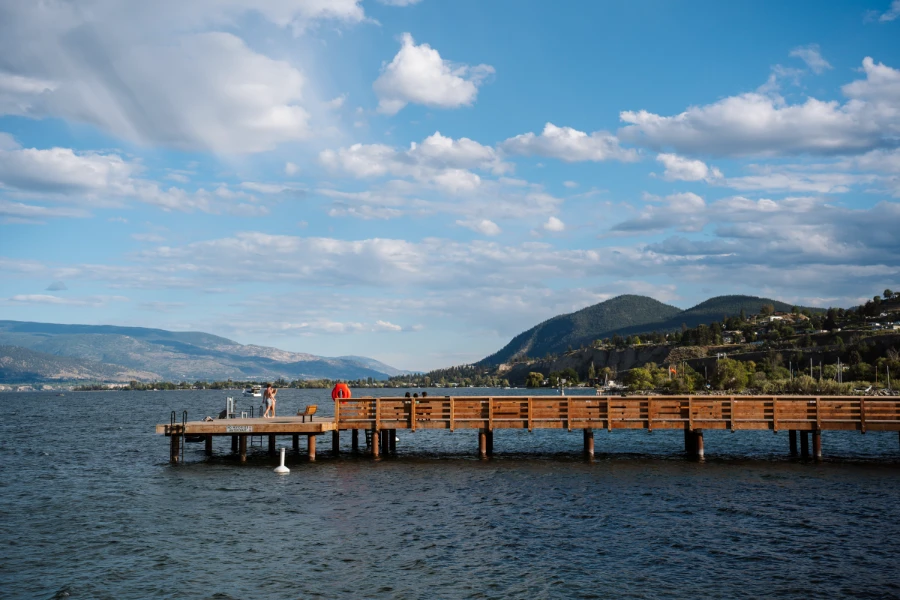 A long wooden dock stretches out over the waters of Okanagan Lake and leads to a flat platform that has several ladders leading into the water and a metal slide at Gordon Beggs Rotary Beach