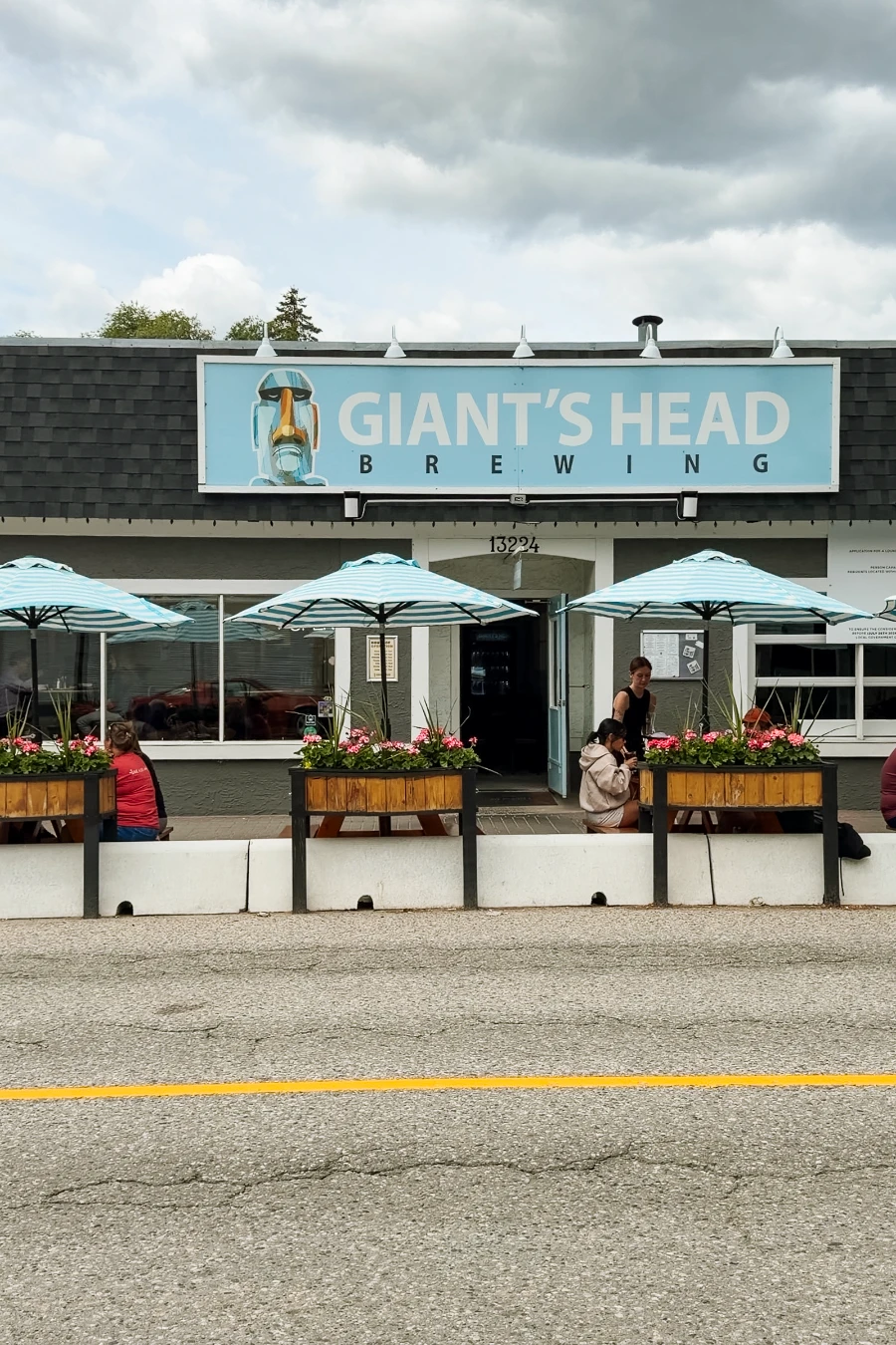 A roadside patio with matched white and blue umbrellas set up in front of a small building with a large sign that reads ‘Giant’s Head Brewing’