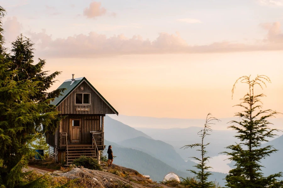 Woman stands next to a wooden hut looking out to sweeping mountain views