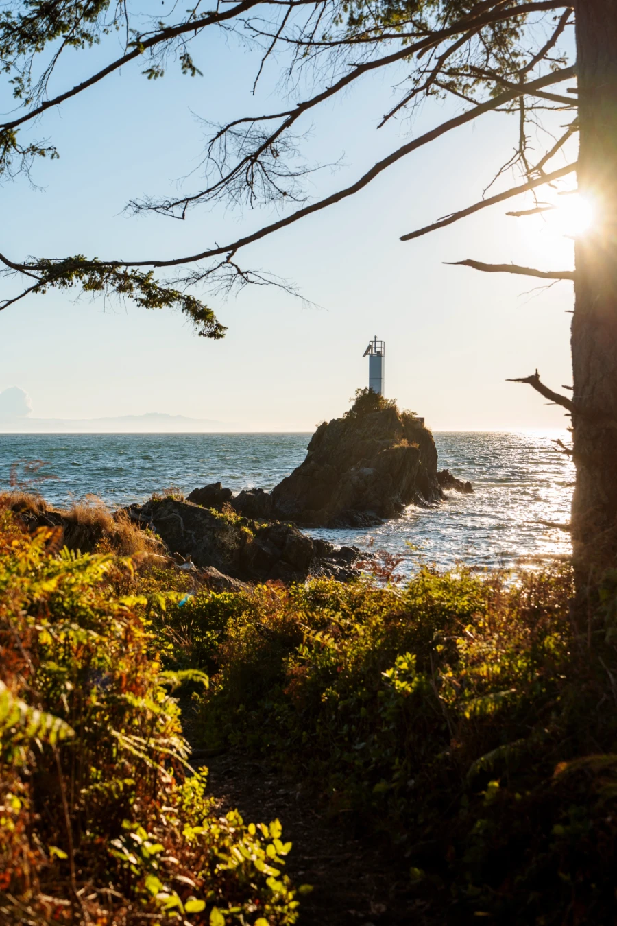 White lighthouse on a rocky outcropping catching some golden light at Lighthouse Lane Park on Bowen Island (At High Tide)