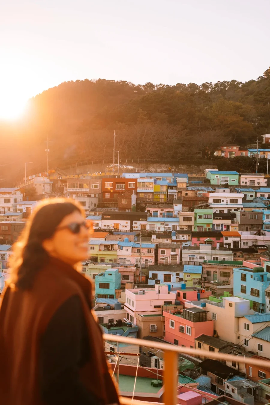Woman stands in front of a viewpoint that looks down at the many colorful houses of Gamcheon Culture Village