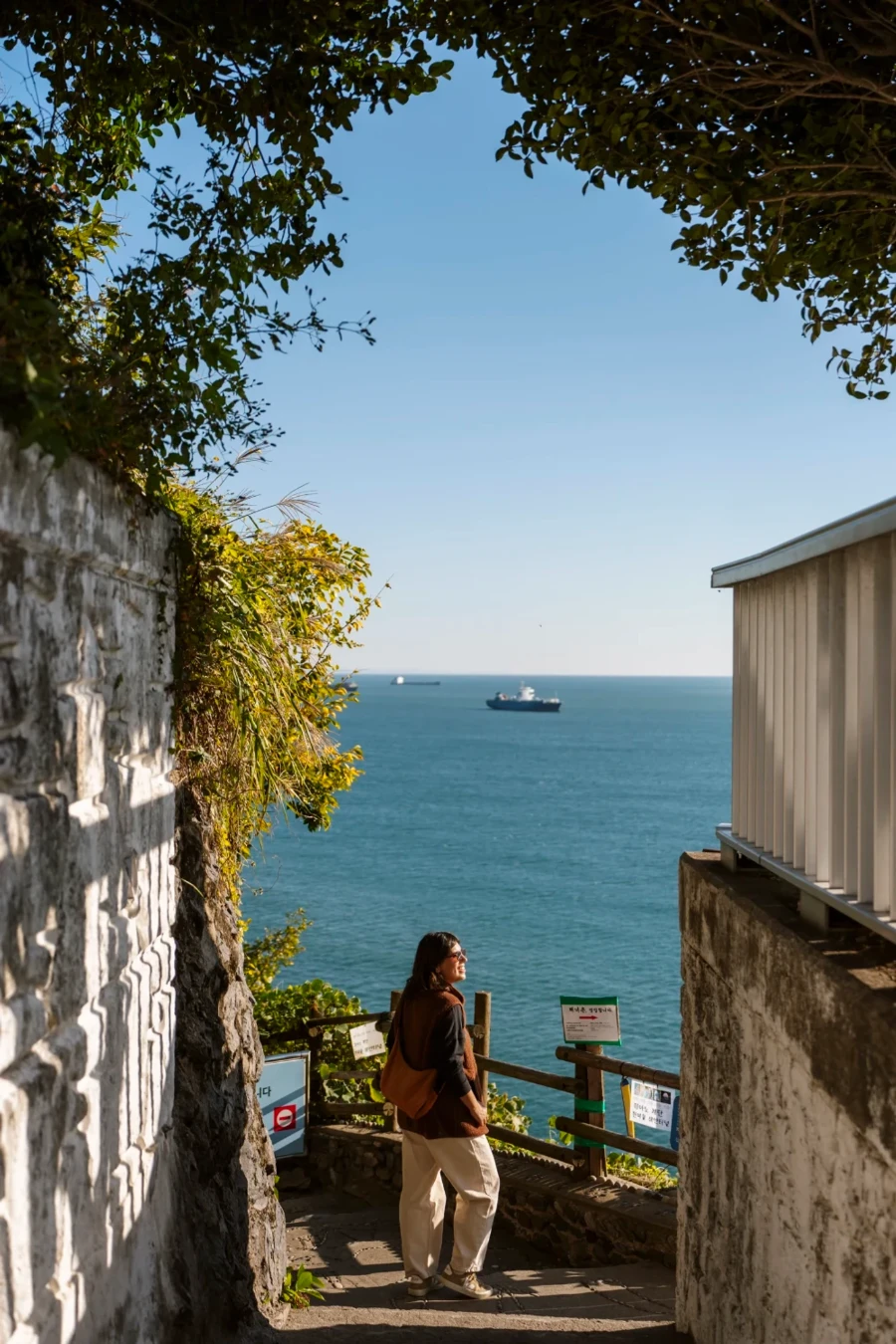 Woman looking out to the ocean where two large ships float on the water at Huinnyeoul Munhwa Maul