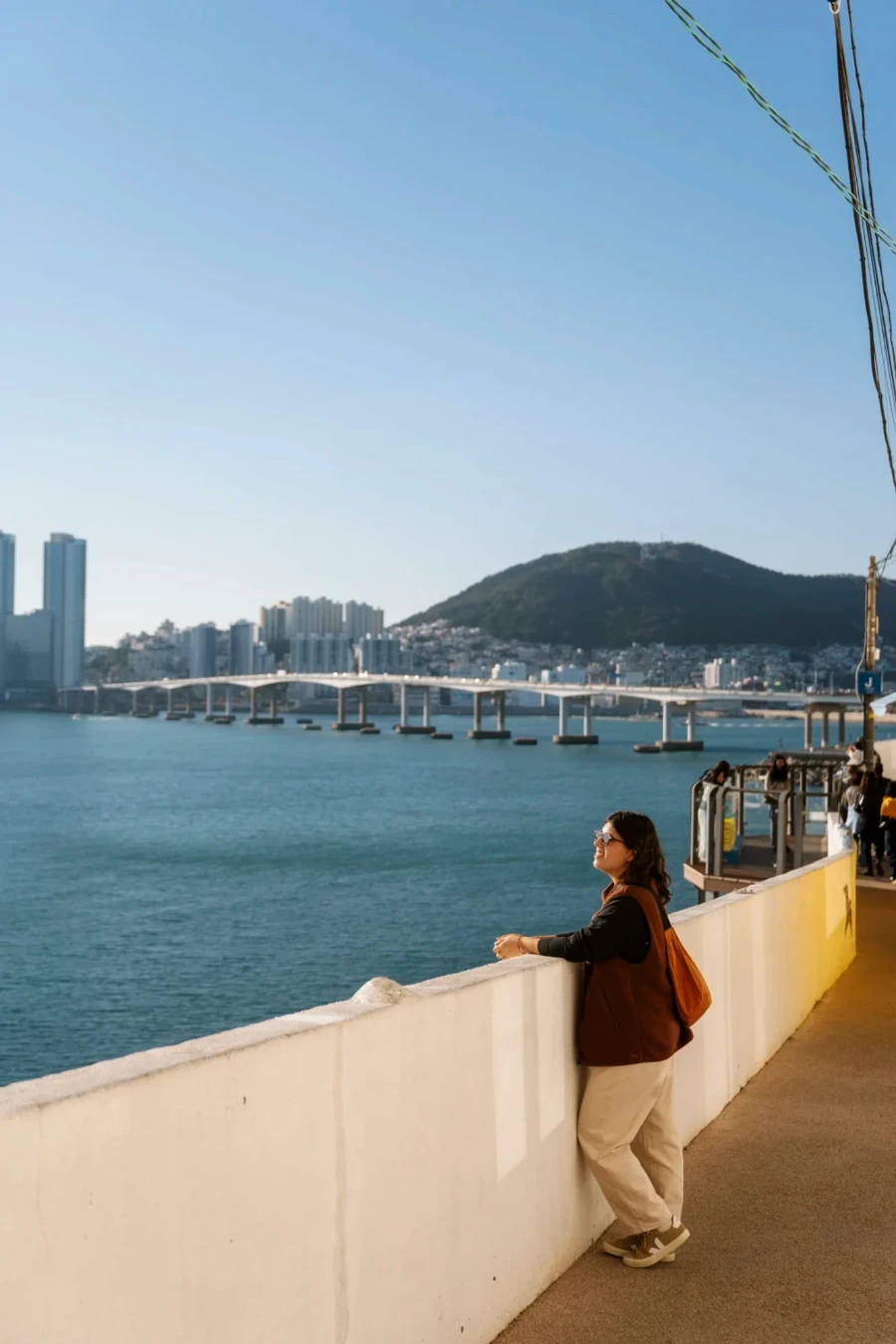 A woman leans against a stone railing along the waters near Busan