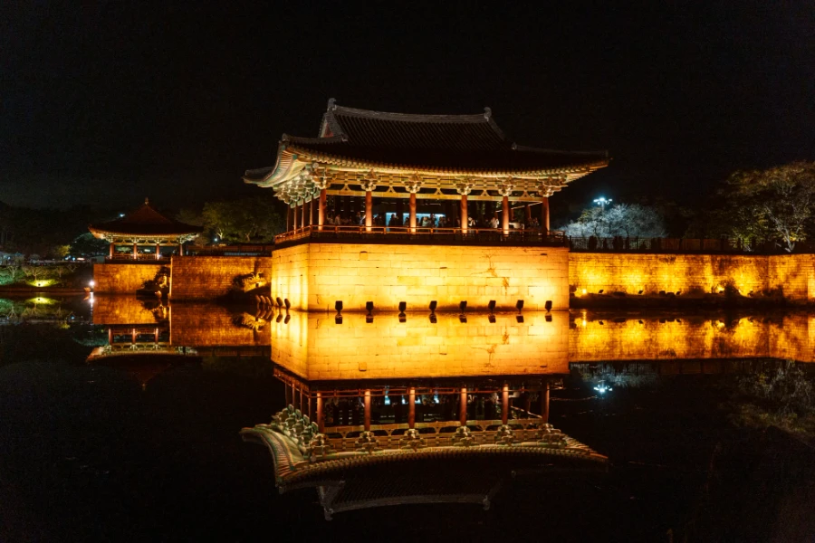 A temple is illuminated by a row of powerful lights causing an immaculate reflection in the water below at Donggung Palace