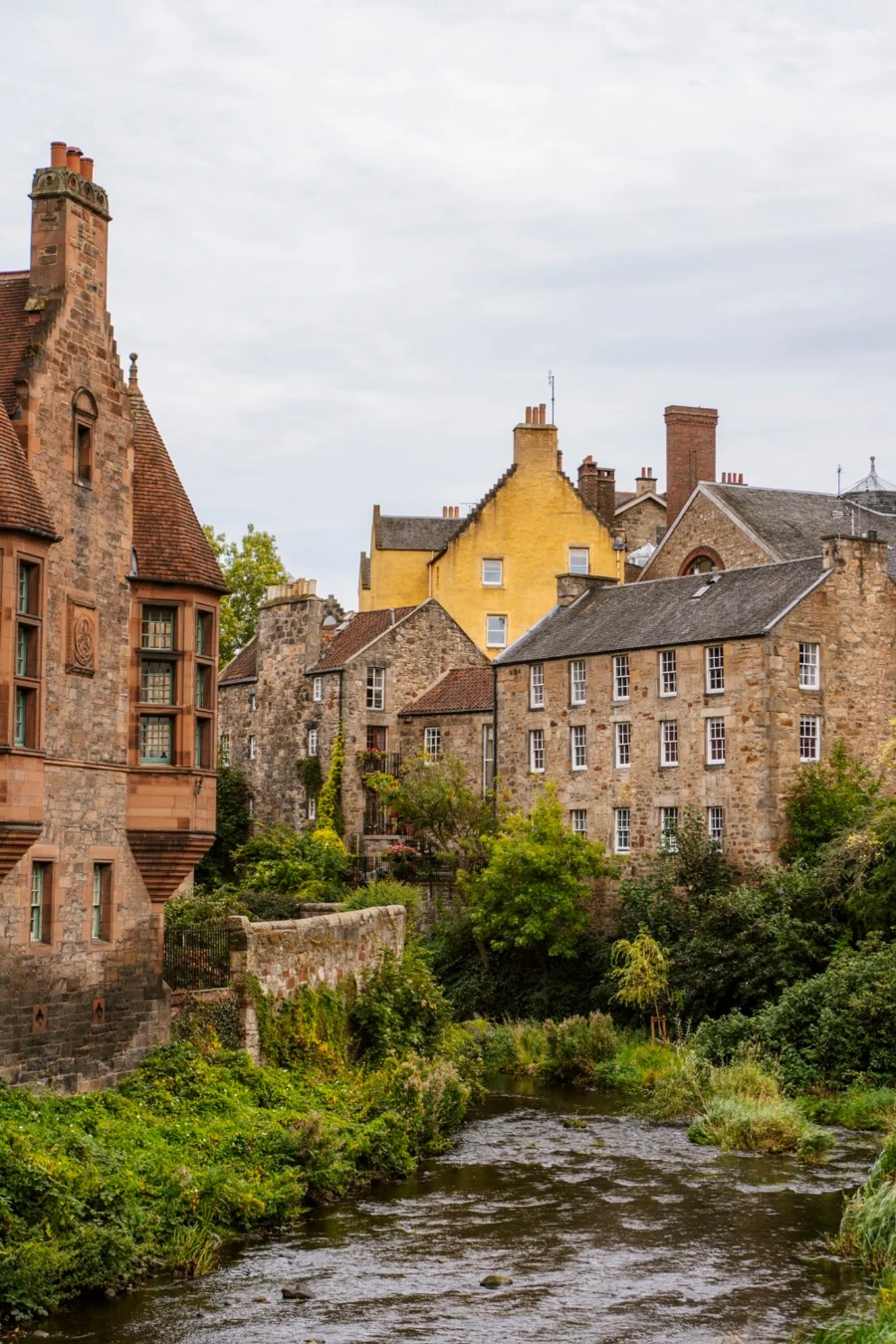 A river lined with green shrubbery and old brown buildings in Dean Village
