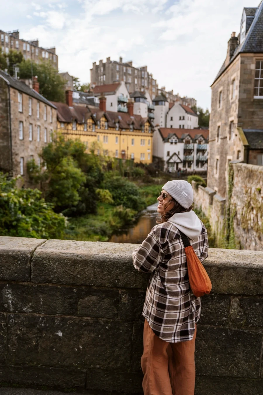 A woman leans of the side of a stone bridge with the waters of Leith flowing underneath